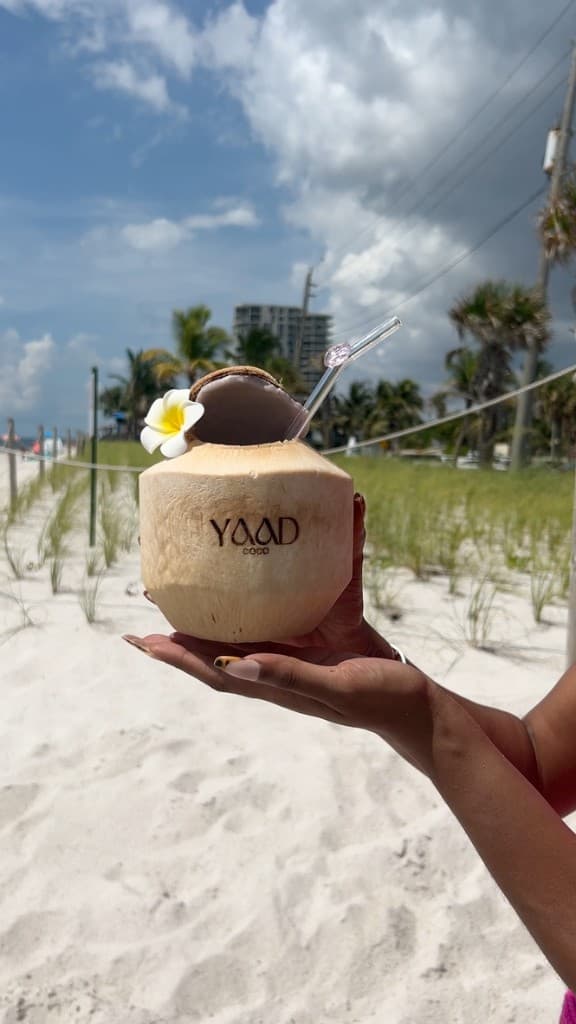 Hands holding a Yaad Coco branded coconut on the beach